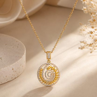 A gold pendant necklace with a spiral design, adorned with zircon, displayed on a warm beige fabric background with decorative stone and dried flowers.